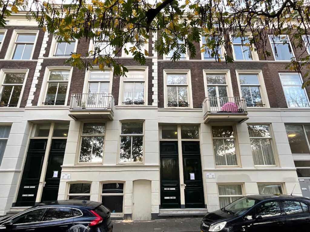 Voorgevel van een historisch pand met balkons en geparkeerde auto's ervoor.