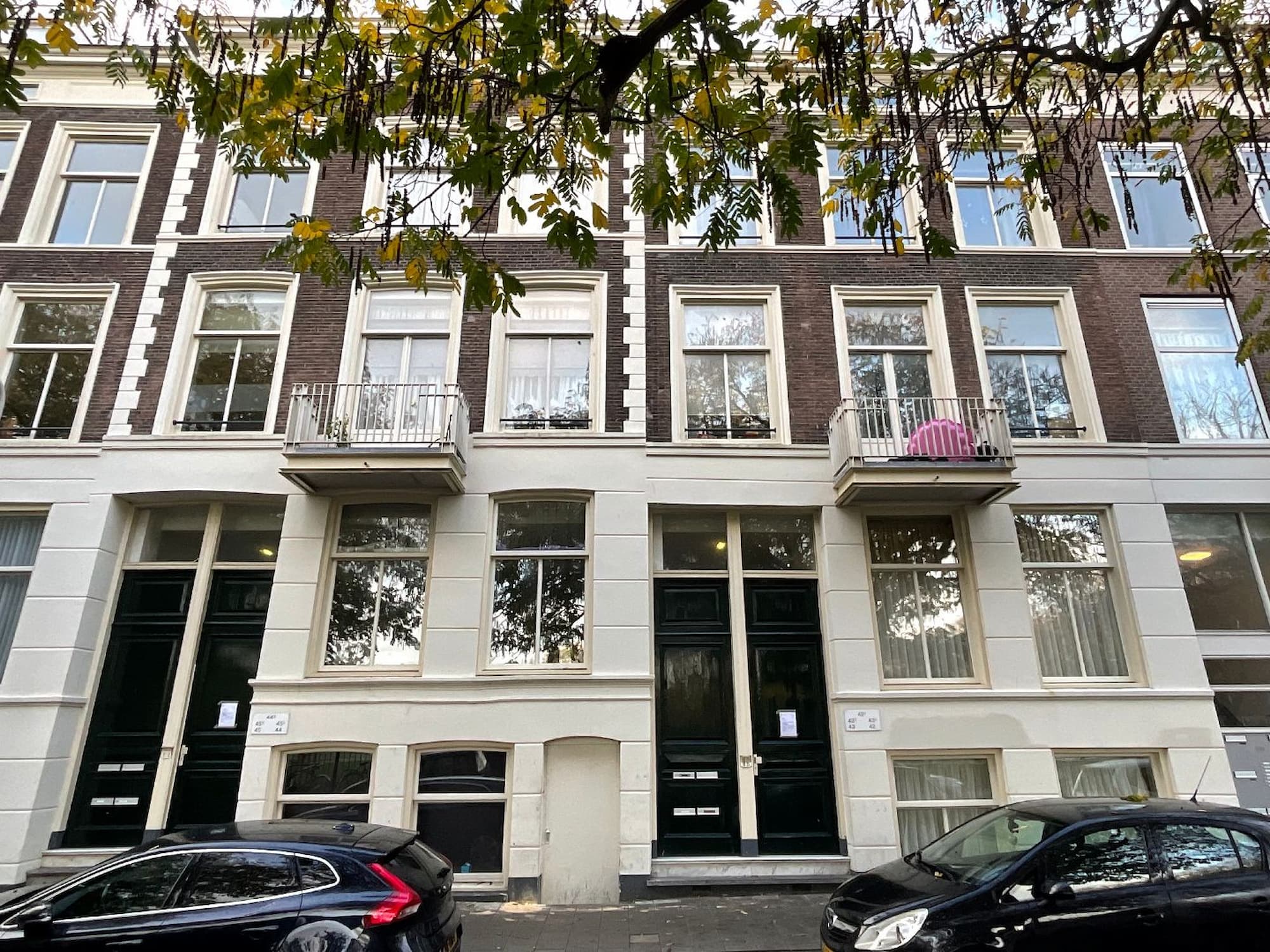 Voorgevel van een historisch pand met balkons en geparkeerde auto's ervoor.