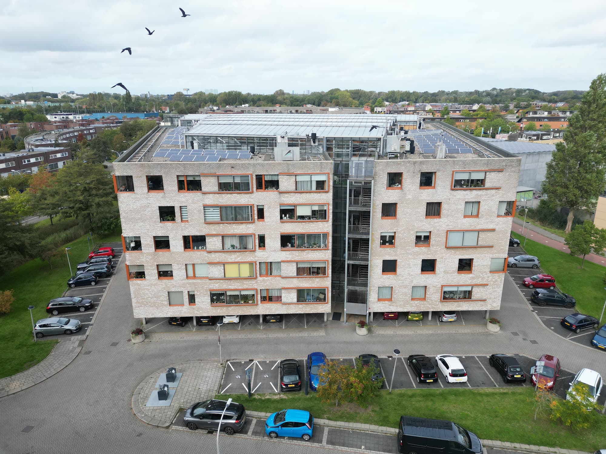 Achtergevel van een modern appartementencomplex met parkeerplaatsen en zonnepanelen op het dak.