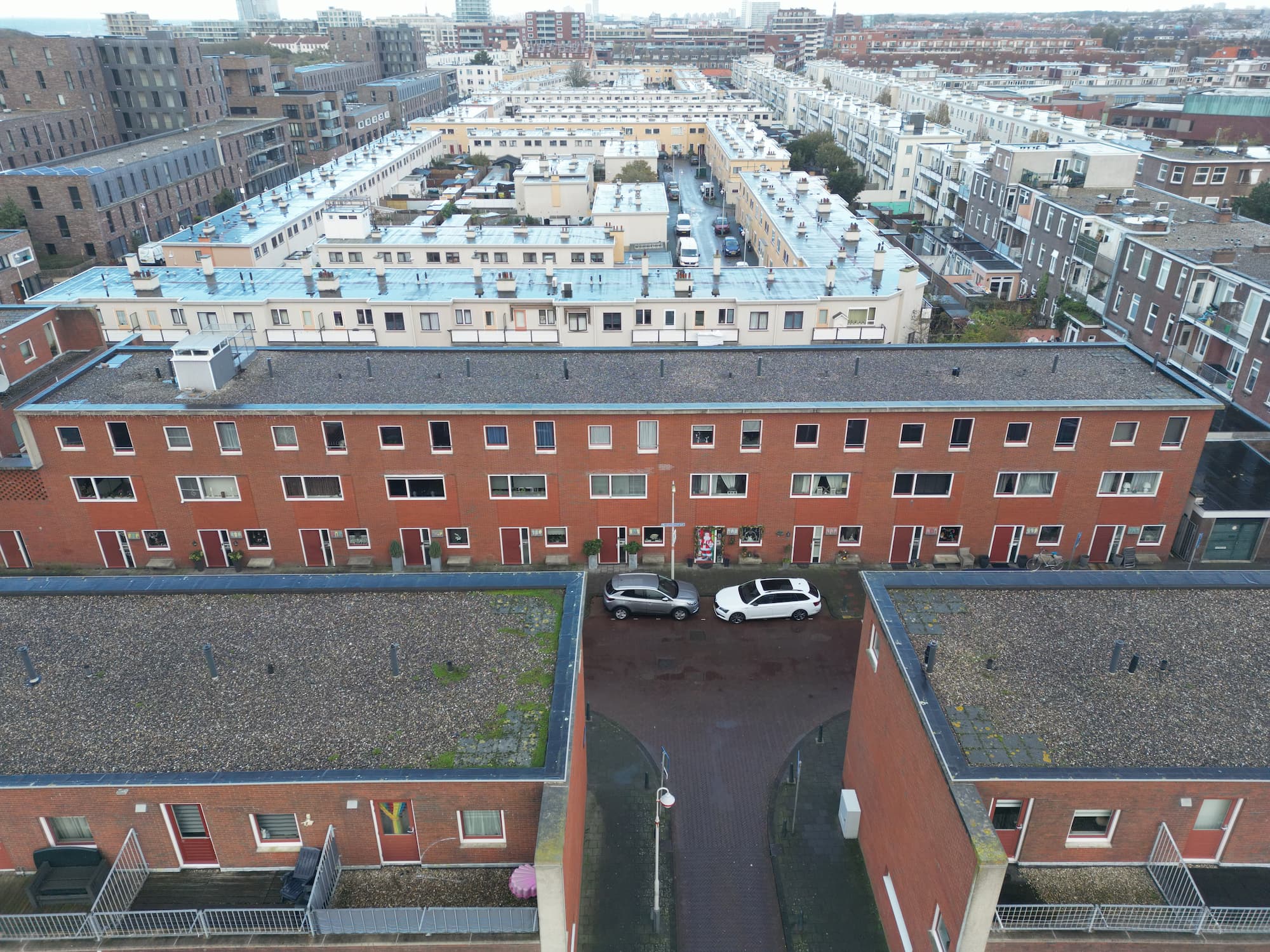 Luchtfoto van de voorgevel van een rijbakstenen huizen in een stedelijke omgeving met parkeerplaatsen.