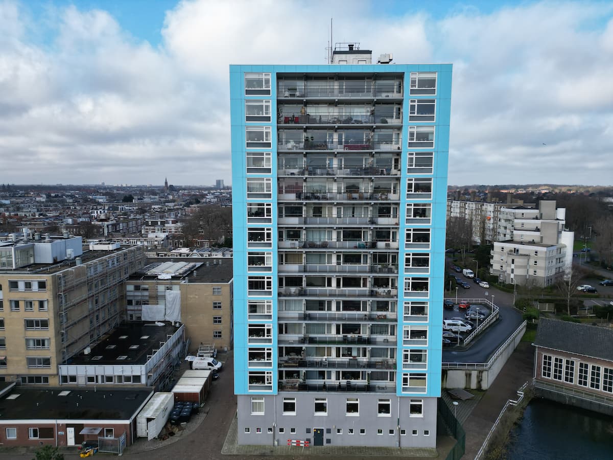 Hoog woonflatgebouw met blauwe omlijsting, gezien vanaf de achterkant, in een stedelijke omgeving.