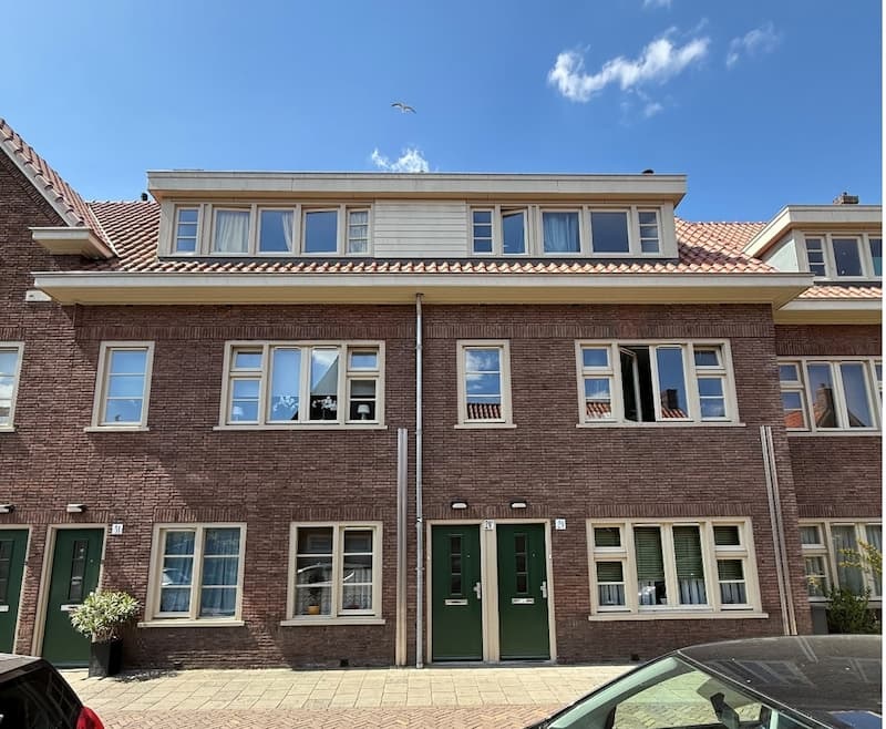 Een rij van karakteristieke rode bakstenen huizen met groene voordeuren onder een blauwe lucht.