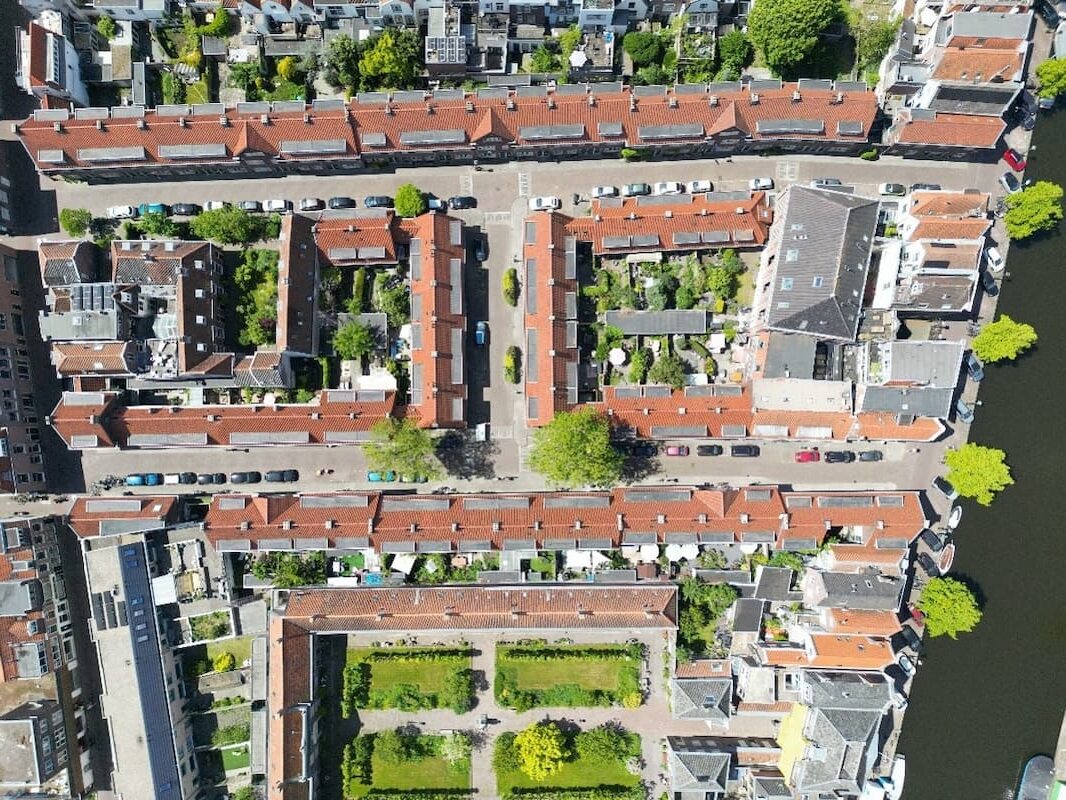 Luchtfoto van een stadsblok met rode daken, groene binnenplaatsen en omliggende straten.