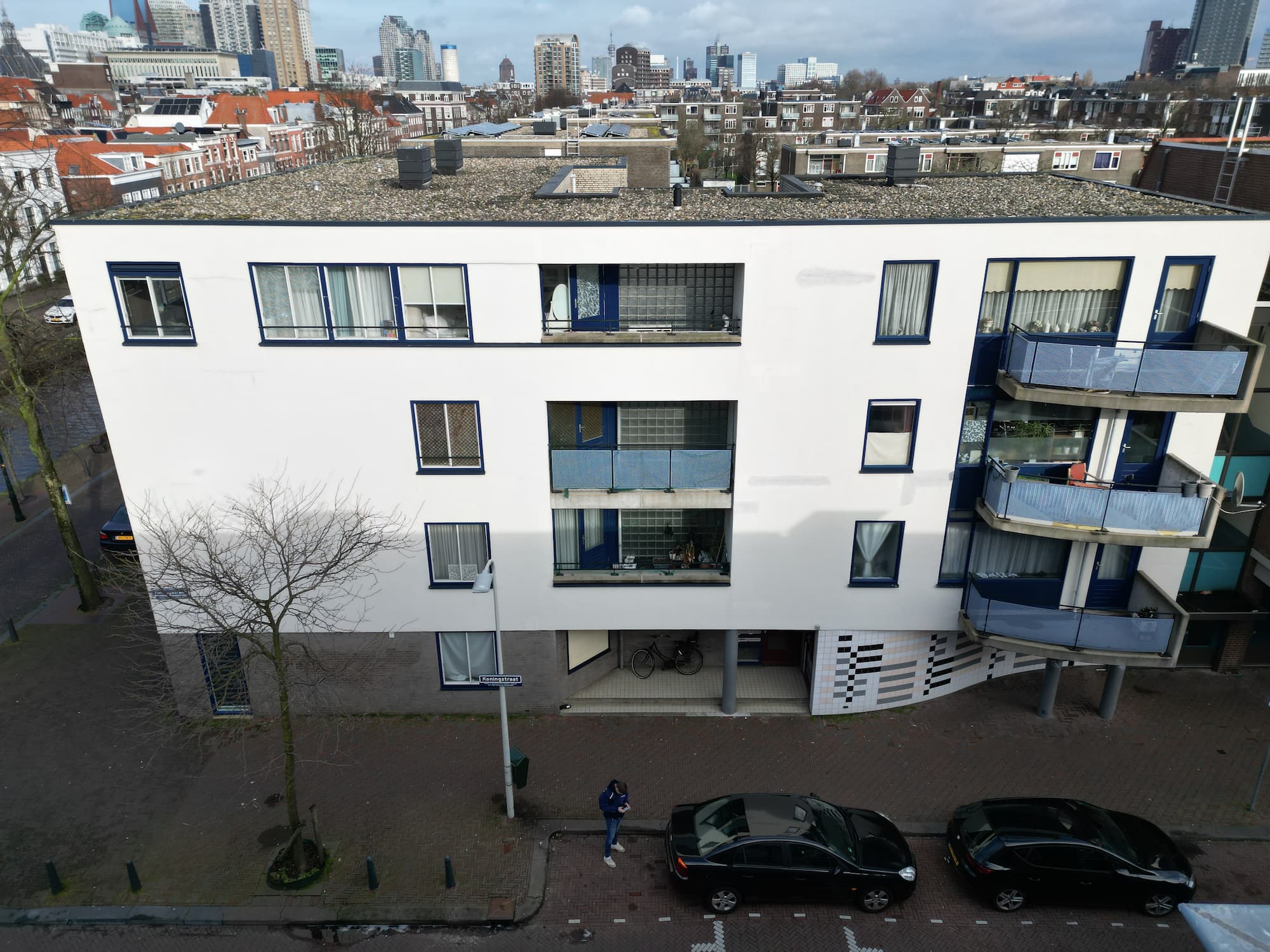 Bovenaanzicht van een modern woongebouw in een stedelijke omgeving, met geparkeerde auto's langs de straat.