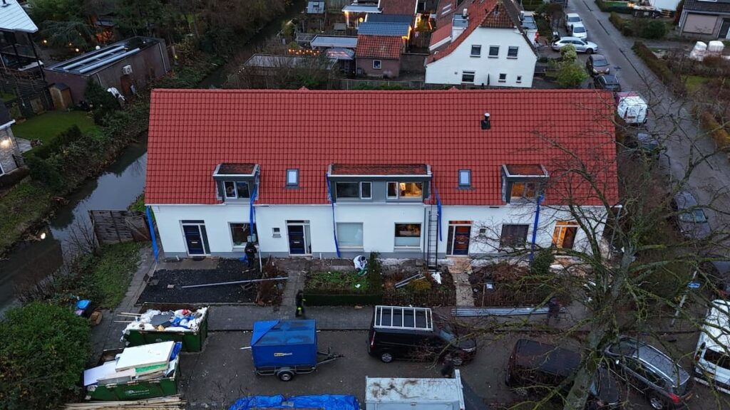 Luchtfoto van een rij nieuwbouwwoningen met rode dakpannen en bouwmaterialen op de oprit.