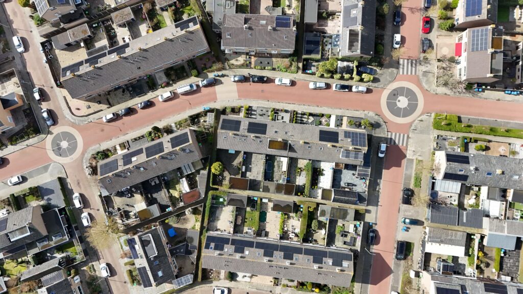 Luchtfoto van een woonwijk met rijenhuizen, tuinen en een kruispunt met rotondes.