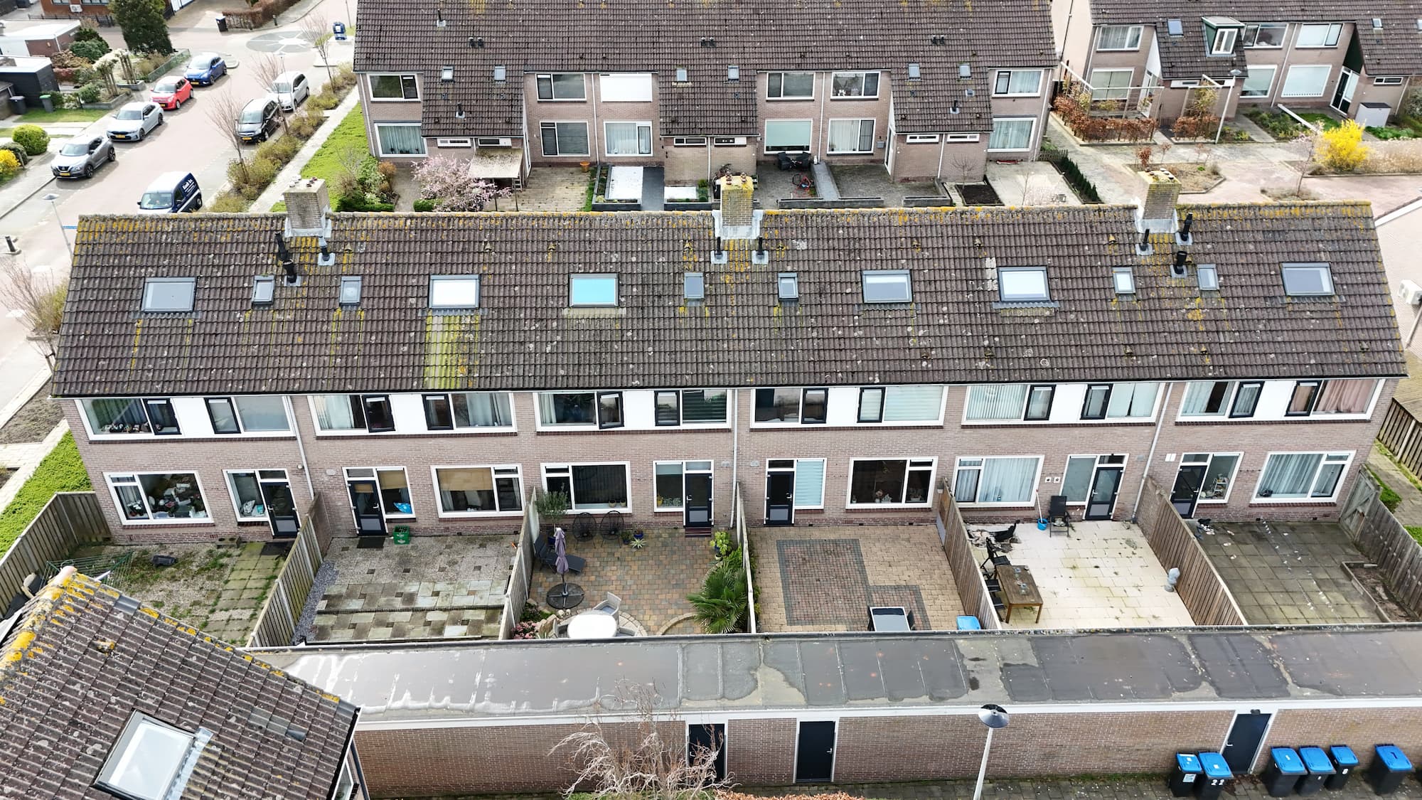 Luchtfoto van een rij bakstenen woningen met achtertuinen in een Nederlandse woonwijk.