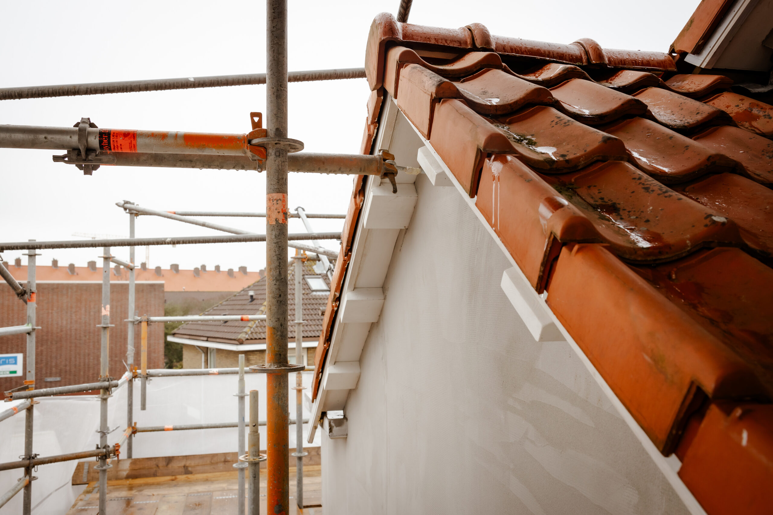 Rode dakpannen en gevel van een woning in de steigers tijdens renovatiewerkzaamheden.