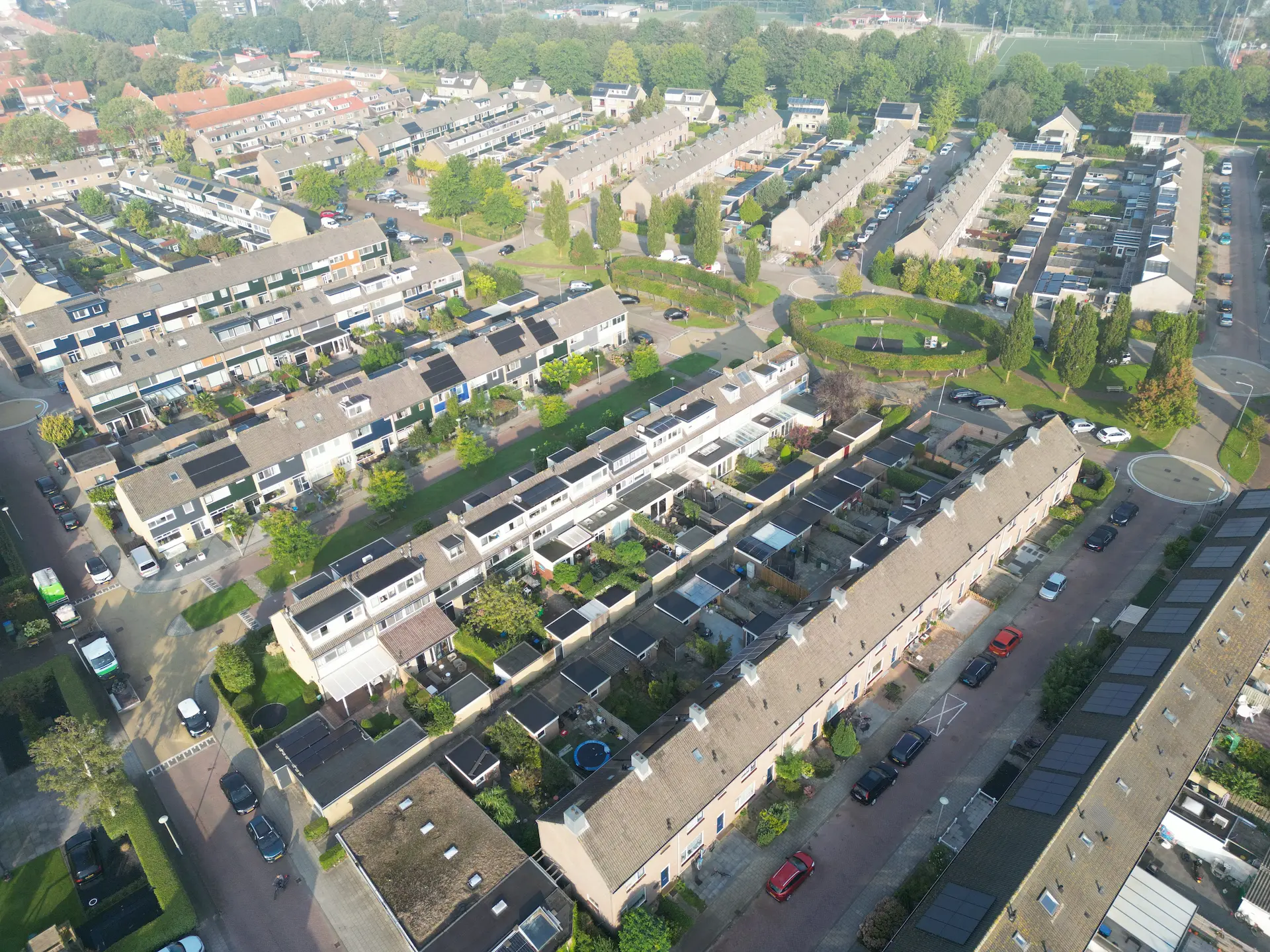 Luchtfoto van een woonwijk met rijtjeshuizen, tuinen en groene zones in een overzichtelijk stratenpatroon.