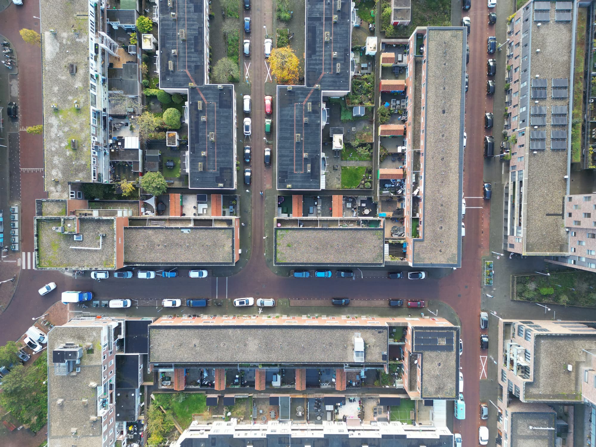 Luchtfoto van een stedelijk gebied met meerdere woongebouwen en geparkeerde auto's langs de straten.